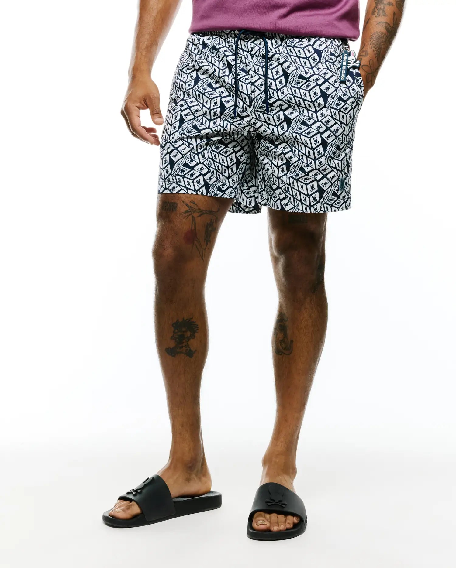 Mens Eddy All Over Print Swim Trunk in navy and white, featuring a classic fit, smooth fabric, and an all-over geometric cube pattern with small Psycho Bunny skull logos. Includes a drawstring waist, branded tag, and small embroidered logo.