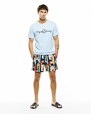 Light blue jersey t-shirt with large Psycho Bunny script logo on chest, paired with Mens Wes All Over Print Swim Trunk featuring a vibrant multi-color abstract pattern and subtle bunny skull logos.
