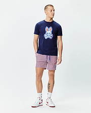 Navy blue jersey t-shirt with a large gradient Psycho Bunny skull logo on the chest, paired with Mens John All Over Print Swim Trunk featuring red, white, and navy vertical stripes and a small embroidered bunny logo.