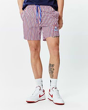 Mens John All Over Print Swim Trunk. Classic fit, red, white, and blue striped swim trunk with a blue drawstring featuring small bunny logos and an embroidered Psycho Bunny skull on the lower left leg.