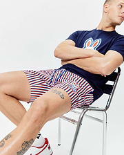 Navy blue jersey t-shirt with a large white, red, and blue Psycho Bunny logo on the chest, paired with Mens John All Over Print Swim Trunk featuring red, white, and blue stripes and a small embroidered bunny logo.