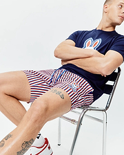 Navy blue jersey t-shirt with a large white, red, and blue Psycho Bunny logo on the chest, paired with Mens John All Over Print Swim Trunk featuring red, white, and blue stripes and a small embroidered bunny logo.