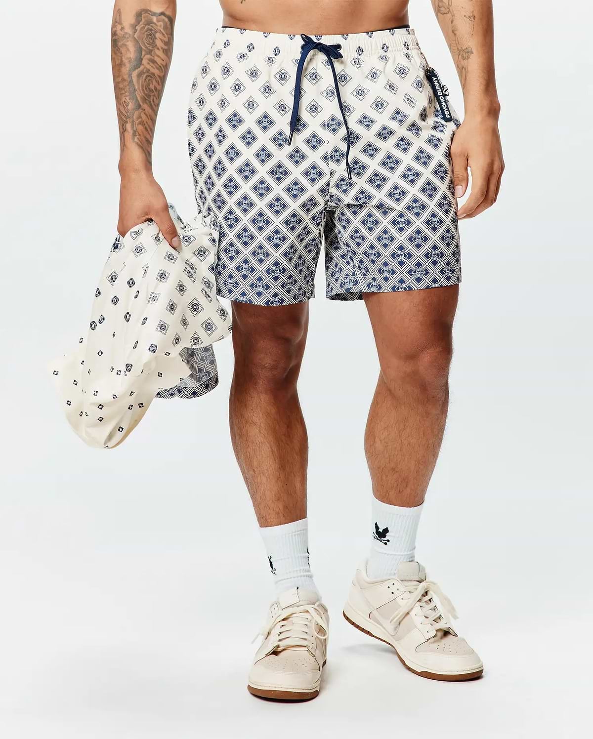 Mens Tobias Swim Trunk in cream with a navy geometric diamond pattern featuring integrated Psycho Bunny skull logos, a navy drawstring, and a branded side tag.