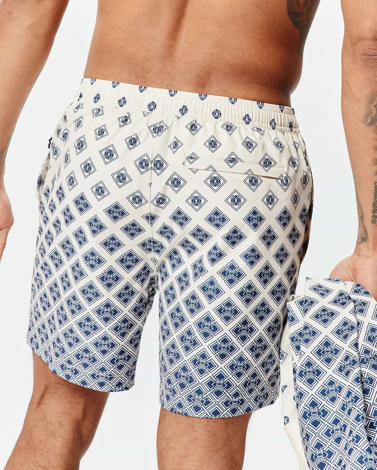 Mens Tobias Swim Trunk in cream with a navy blue all-over geometric pattern featuring the small Psycho Bunny skull logo, classic fit, smooth quick-dry fabric, and a back pocket.