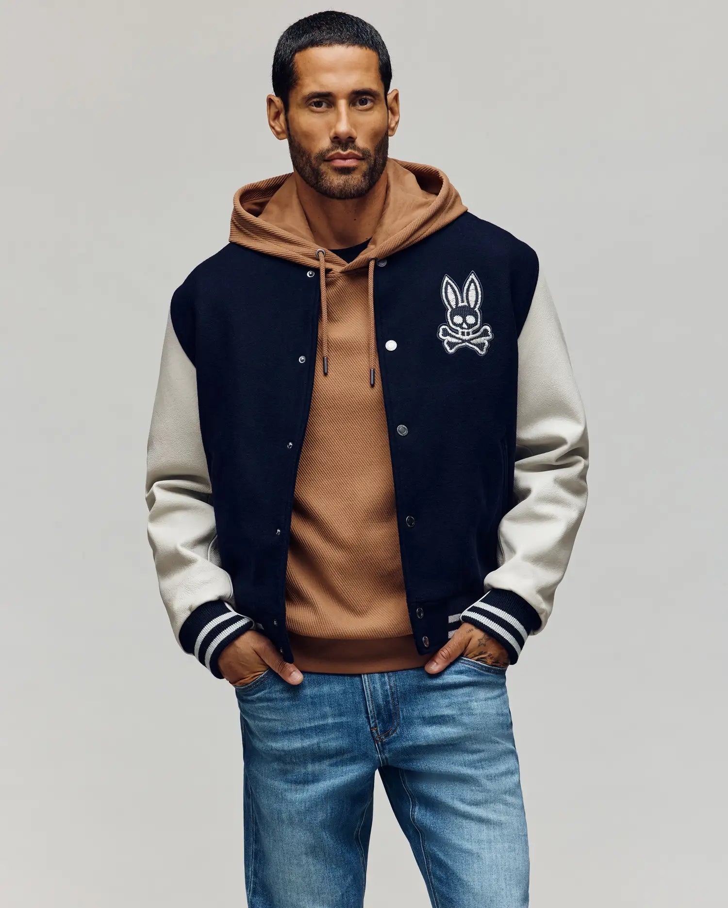Mens Jacob Leather Bomber in classic fit, featuring a navy wool blend body with cream leather sleeves, snap closure, and ribbed cuffs. A large white embroidered Psycho Bunny skull logo adorns the left chest.
