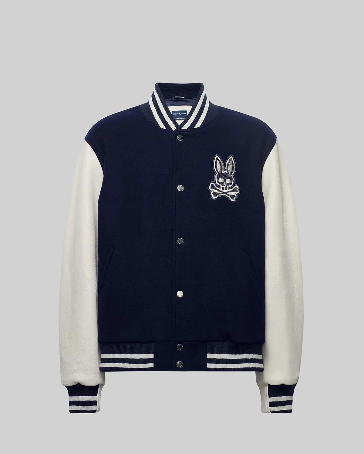 Mens Jacob Leather Bomber in navy with cream leather sleeves, featuring a large embroidered Psycho Bunny skull logo on the left chest, snap buttons, and white striped ribbed knit trim.