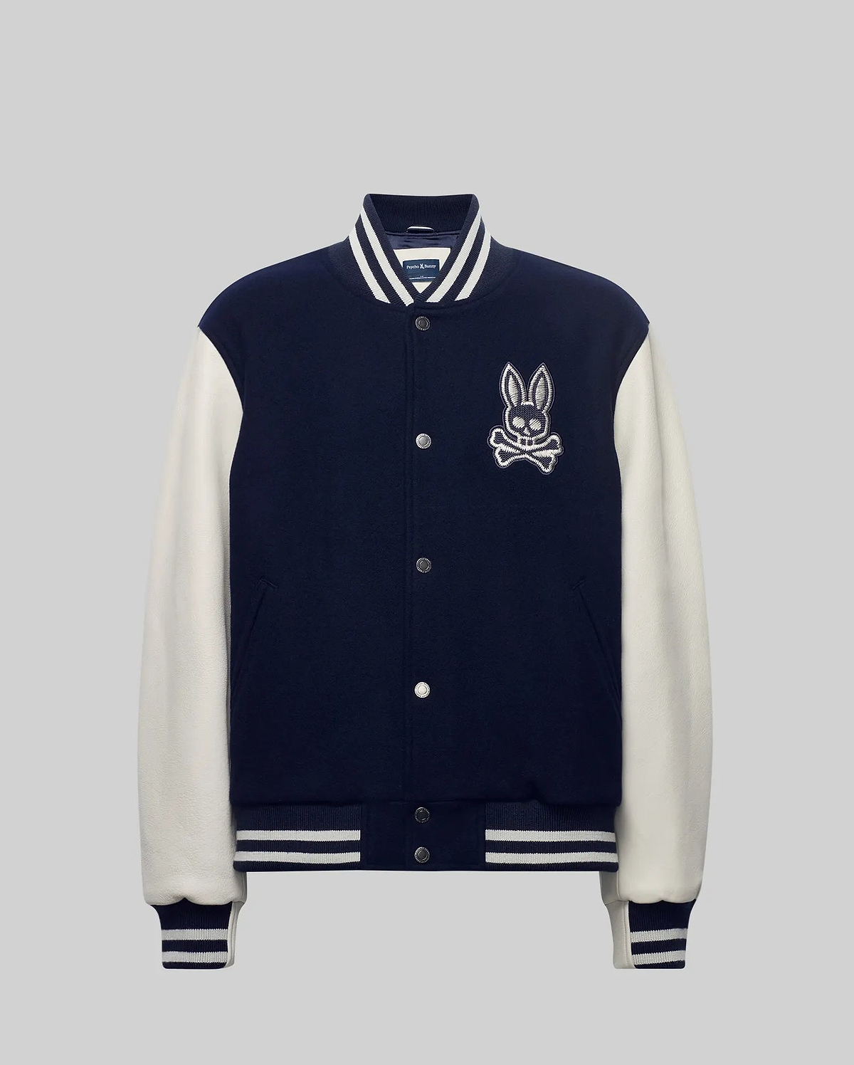 Mens Jacob Leather Bomber in navy with cream leather sleeves, featuring a large embroidered Psycho Bunny skull logo on the left chest, snap buttons, and white striped ribbed knit trim.