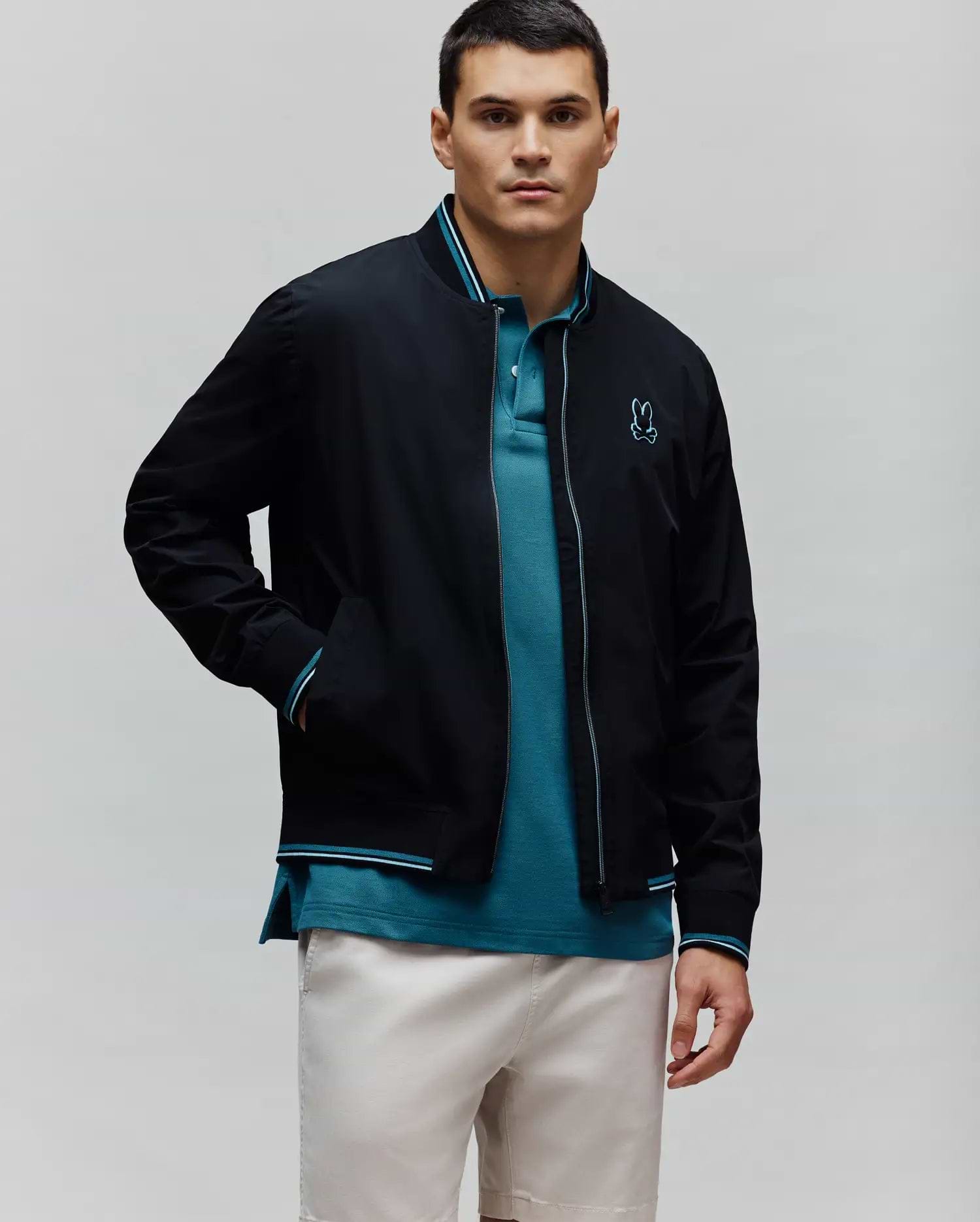 Black Mens Aldrin Bomber jacket with teal and white striped ribbed collar, cuffs, and hem, featuring a full zip with teal trim and a small embroidered teal Psycho Bunny skull logo on the left chest.