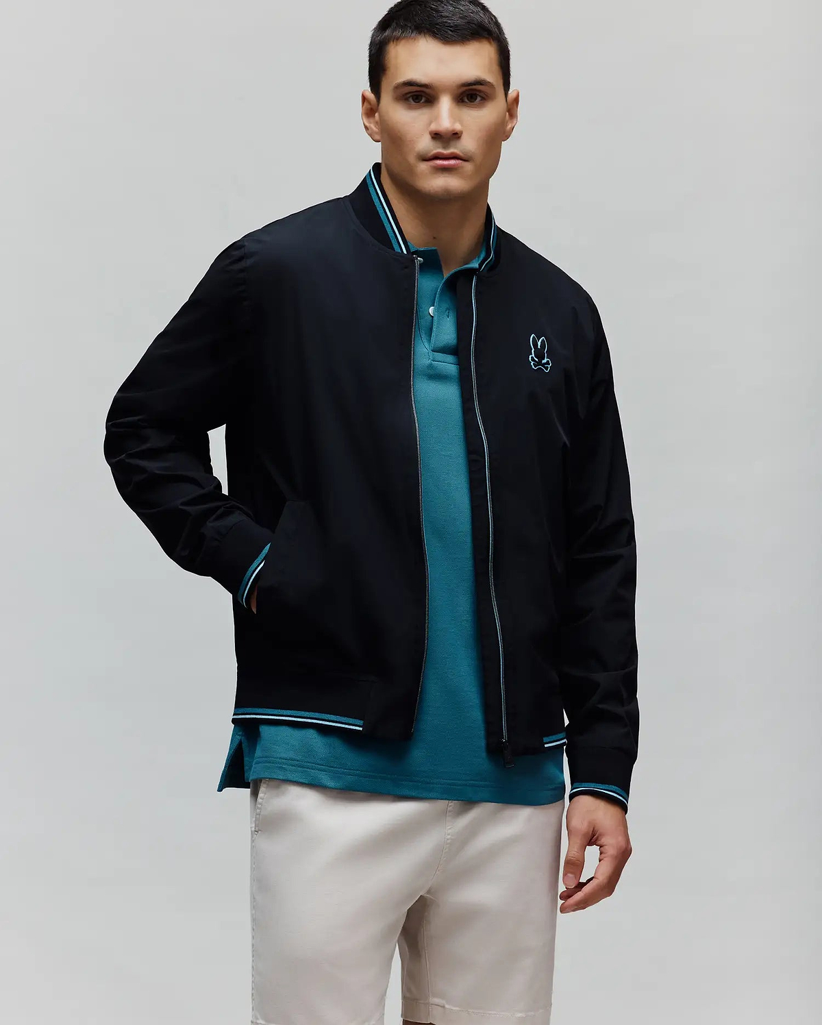 Black Mens Aldrin Bomber jacket with teal and white striped ribbed collar, cuffs, and hem, featuring a full zip with teal trim and a small embroidered teal Psycho Bunny skull logo on the left chest.