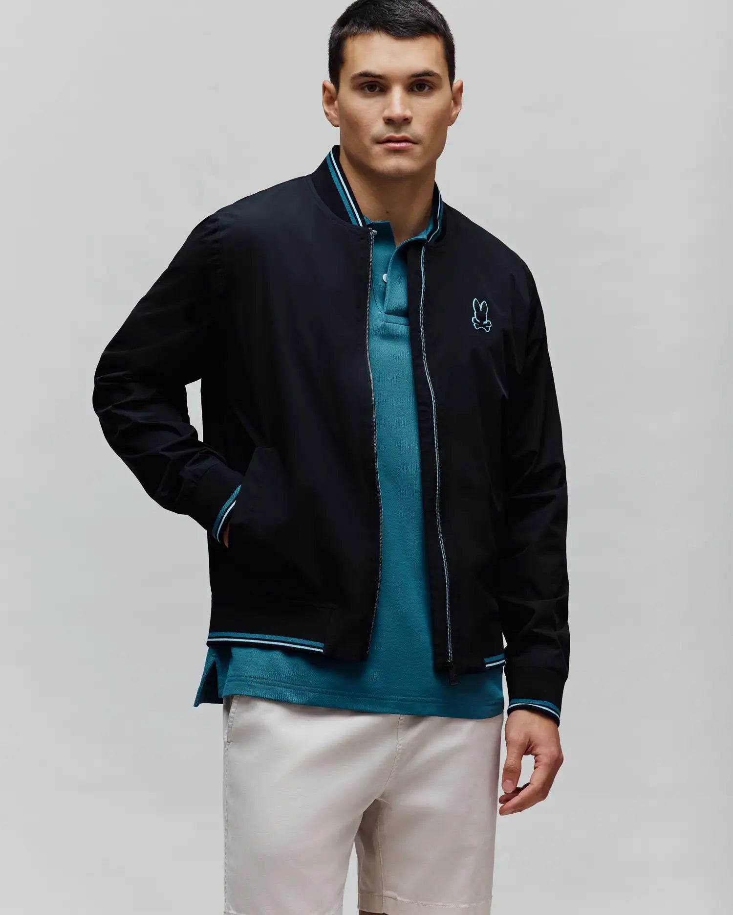 Black Mens Aldrin Bomber jacket with teal and white striped ribbed collar, cuffs, and hem, featuring a full zip with teal trim and a small embroidered teal Psycho Bunny skull logo on the left chest.