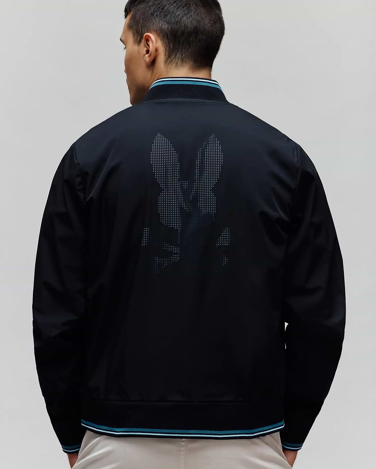 Black Mens Aldrin Bomber with a large pixelated Psycho Bunny skull logo on the back, featuring ribbed collar, cuffs, and hem with teal and white stripes. Smooth fabric, classic fit.