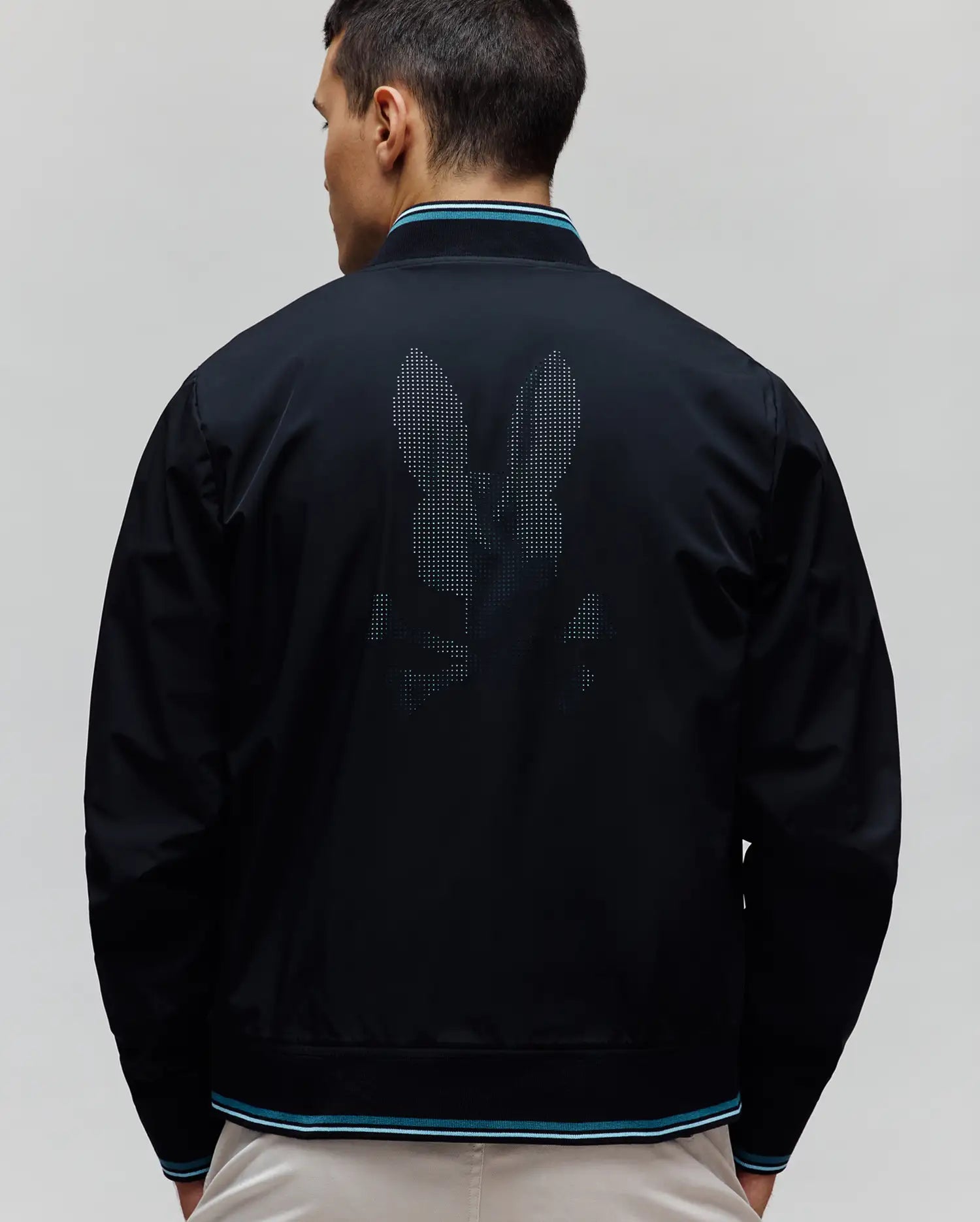 Black Mens Aldrin Bomber with a large pixelated Psycho Bunny skull logo on the back, featuring ribbed collar, cuffs, and hem with teal and white stripes. Smooth fabric, classic fit.