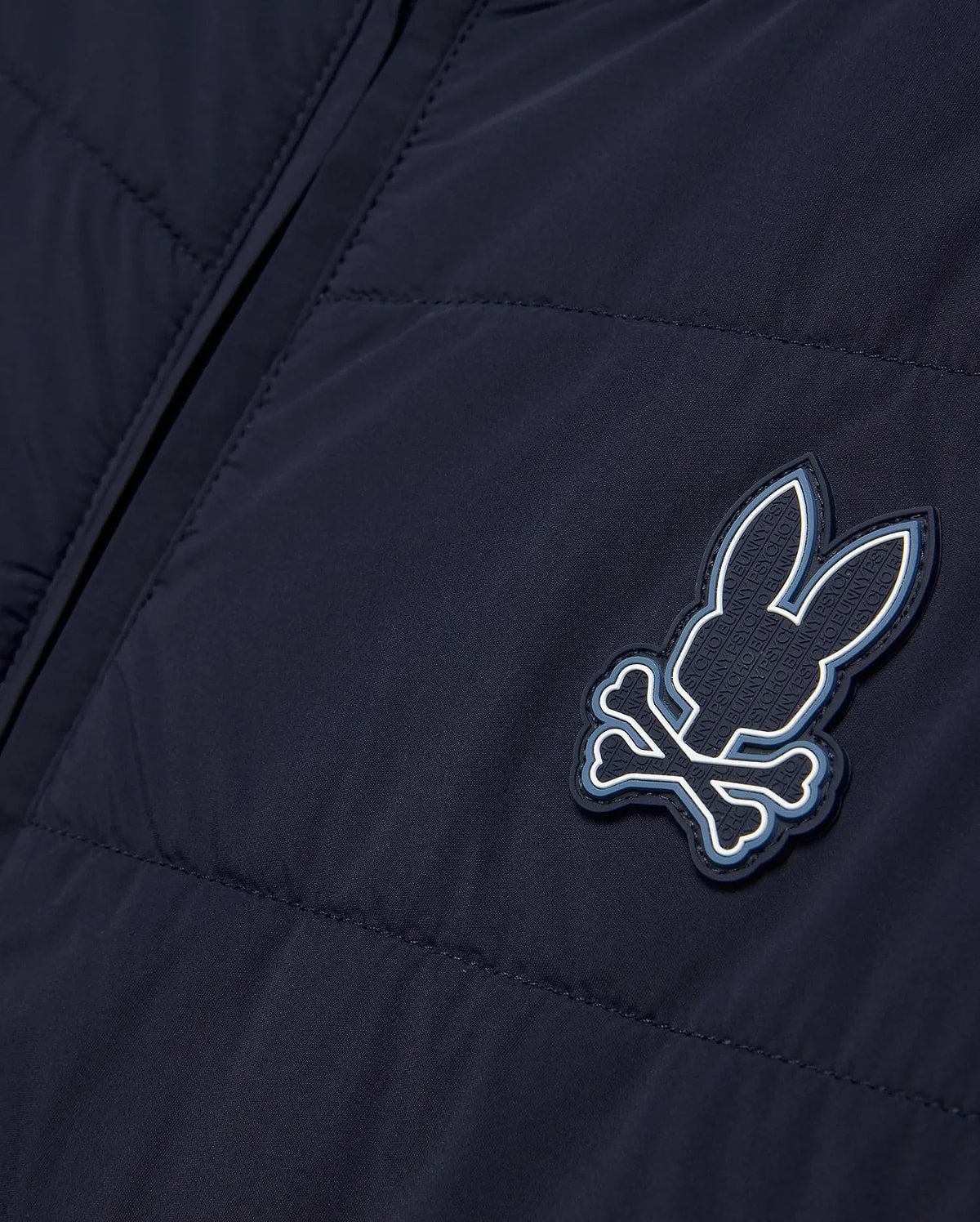 Mens Gordley Mix Media Jacket in navy blue, featuring a quilted left panel and smooth right panel, with a prominent Psycho Bunny skull and crossbones logo on the chest, detailed with white and light blue accents and embossed brand lettering. (5)