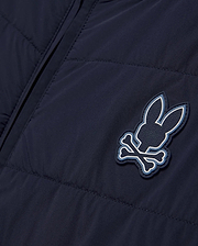 Mens Gordley Mix Media Jacket in navy blue, featuring a quilted left panel and smooth right panel, with a prominent Psycho Bunny skull and crossbones logo on the chest, detailed with white and light blue accents and embossed brand lettering. (5)
