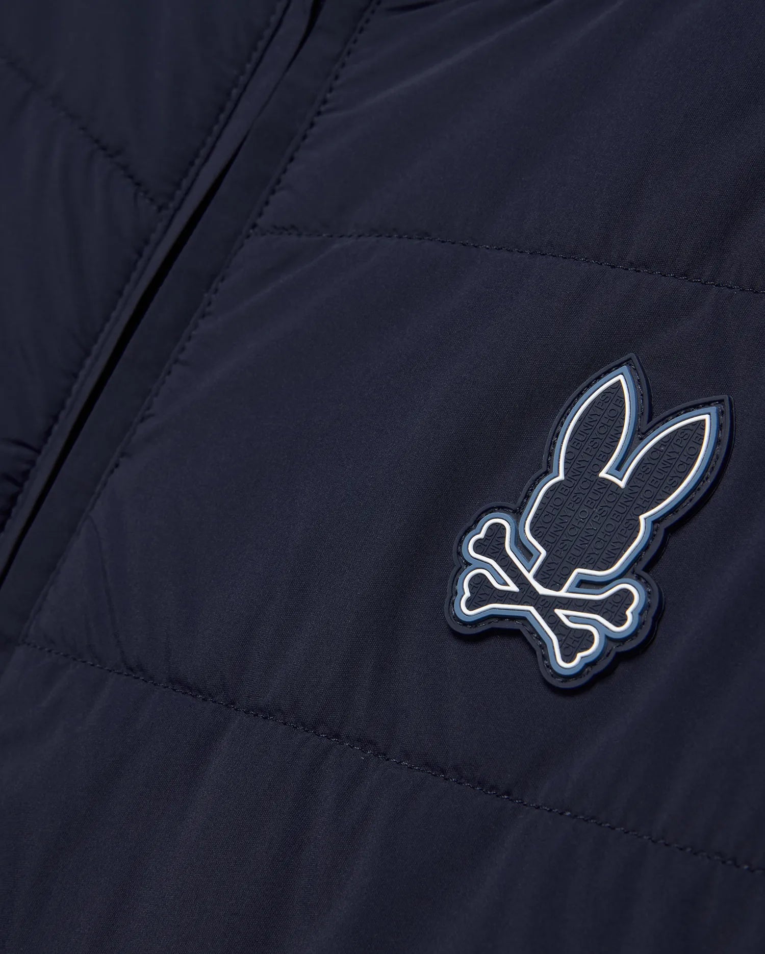 Mens Gordley Mix Media Jacket in navy blue, featuring a quilted left panel and smooth right panel, with a prominent Psycho Bunny skull and crossbones logo on the chest, detailed with white and light blue accents and embossed brand lettering. (5)
