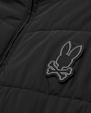 Mens Gordley Mix Media Jacket, black quilted outerwear with a prominent grey and white Psycho Bunny skull logo on the chest, featuring subtle repeating brand text within its design. (6)