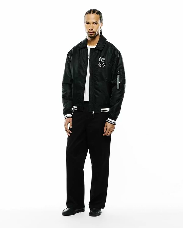 Mens Nathaniel Satin Coach Jacket in black, featuring a relaxed fit, large white embroidered Psycho Bunny skull logo on the left chest, white striped ribbed cuffs, and a Psycho Bunny branded tag on the sleeve. (4)
