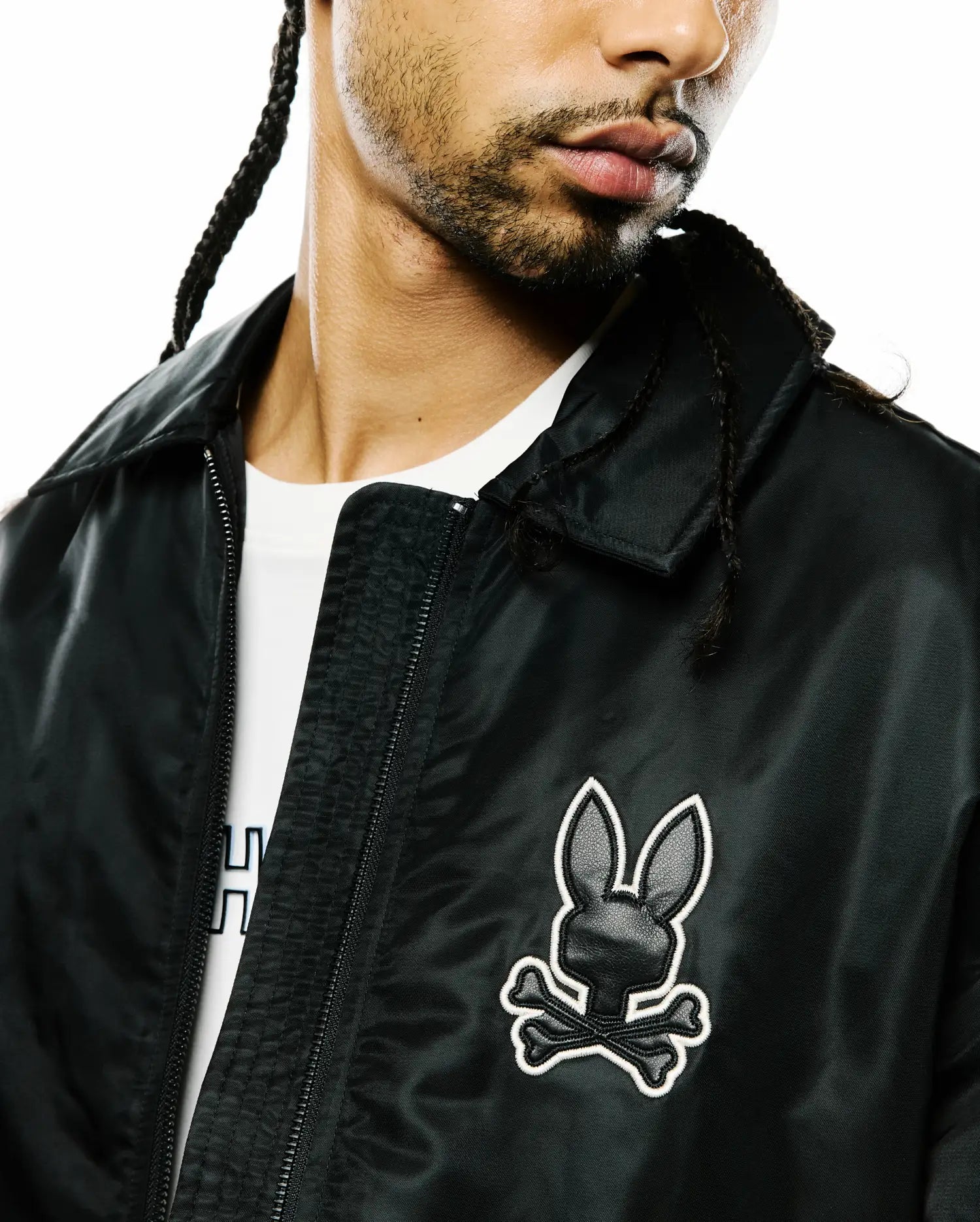 Mens Nathaniel Satin Coach Jacket, black with a subtle sheen, featuring a prominent embroidered Psycho Bunny skull logo on the left chest with white outline and black textured fill, and a full zip. (3)