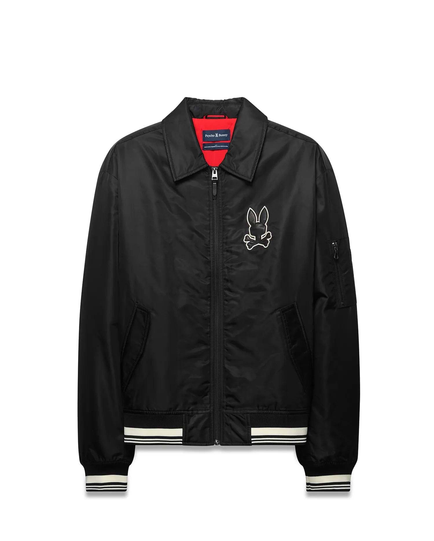 Mens Nathaniel Satin Coach Jacket, black with red lining, featuring a large white embroidered Psycho Bunny skull logo on the chest, white striped ribbed cuffs and hem, and a zippered sleeve pocket. (5)