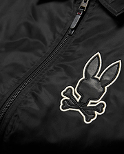 Mens Nathaniel Satin Coach Jacket in black, featuring a prominent embroidered Psycho Bunny skull logo on the chest with black leather-like texture and a white outline, alongside a black zipper. (6)