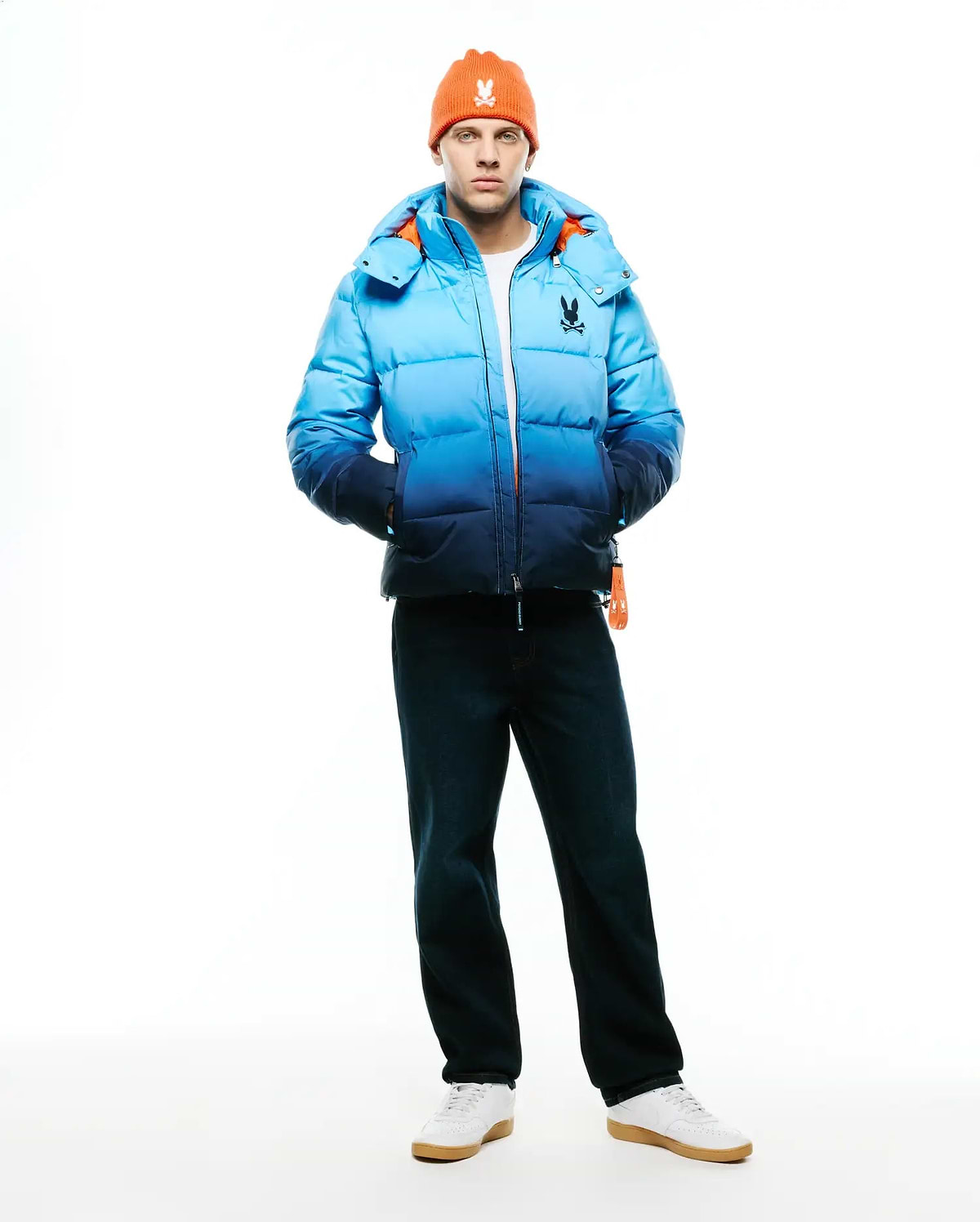 Men's Solan Puffer Jacket, a classic fit quilted puffer jacket featuring a blue ombre design from light to dark, with a vibrant orange interior lining and a small embroidered Psycho Bunny skull logo on the left chest. (4)