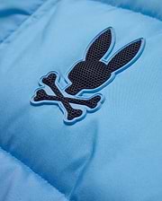 Men's Solan Puffer Jacket in sky blue, featuring a smooth, padded nylon texture and a rubberized dark grey Psycho Bunny skull logo with a light blue outline on the chest. (6)
