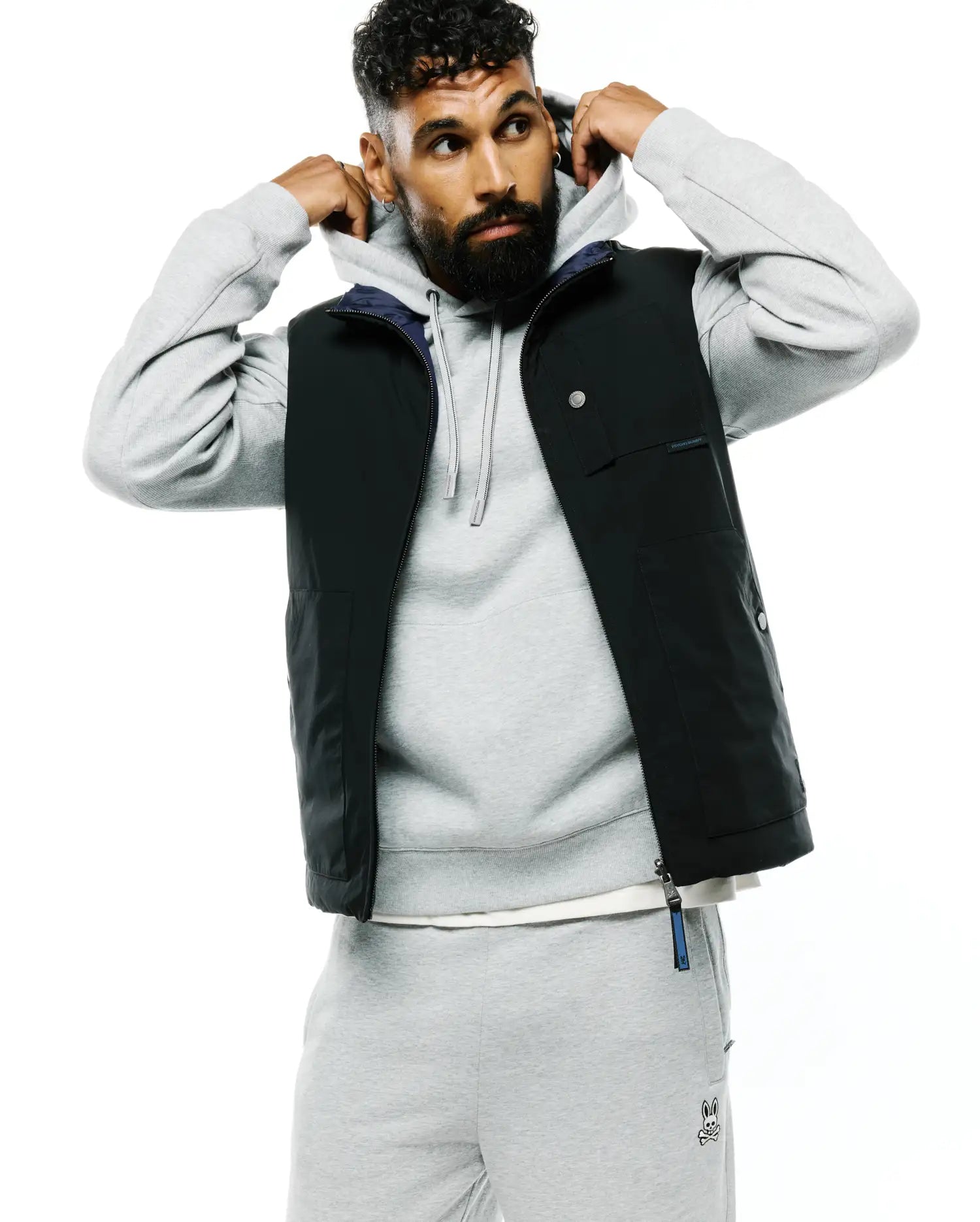 Mens Gordler Reversible Vest, a classic fit black vest with a smooth finish, featuring a navy interior, full zip, snap-button chest pockets, and a Psycho Bunny text label on the chest with a branded zipper pull.