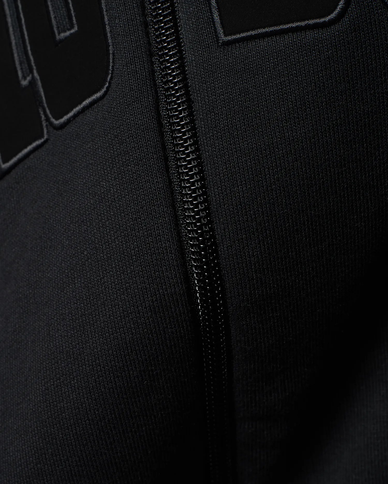 Mens Joaquin Mix Media Reversible Bomber in black, showcasing large raised black letters with a subtle grey outline on a smooth knit fabric, alongside a black front zipper.