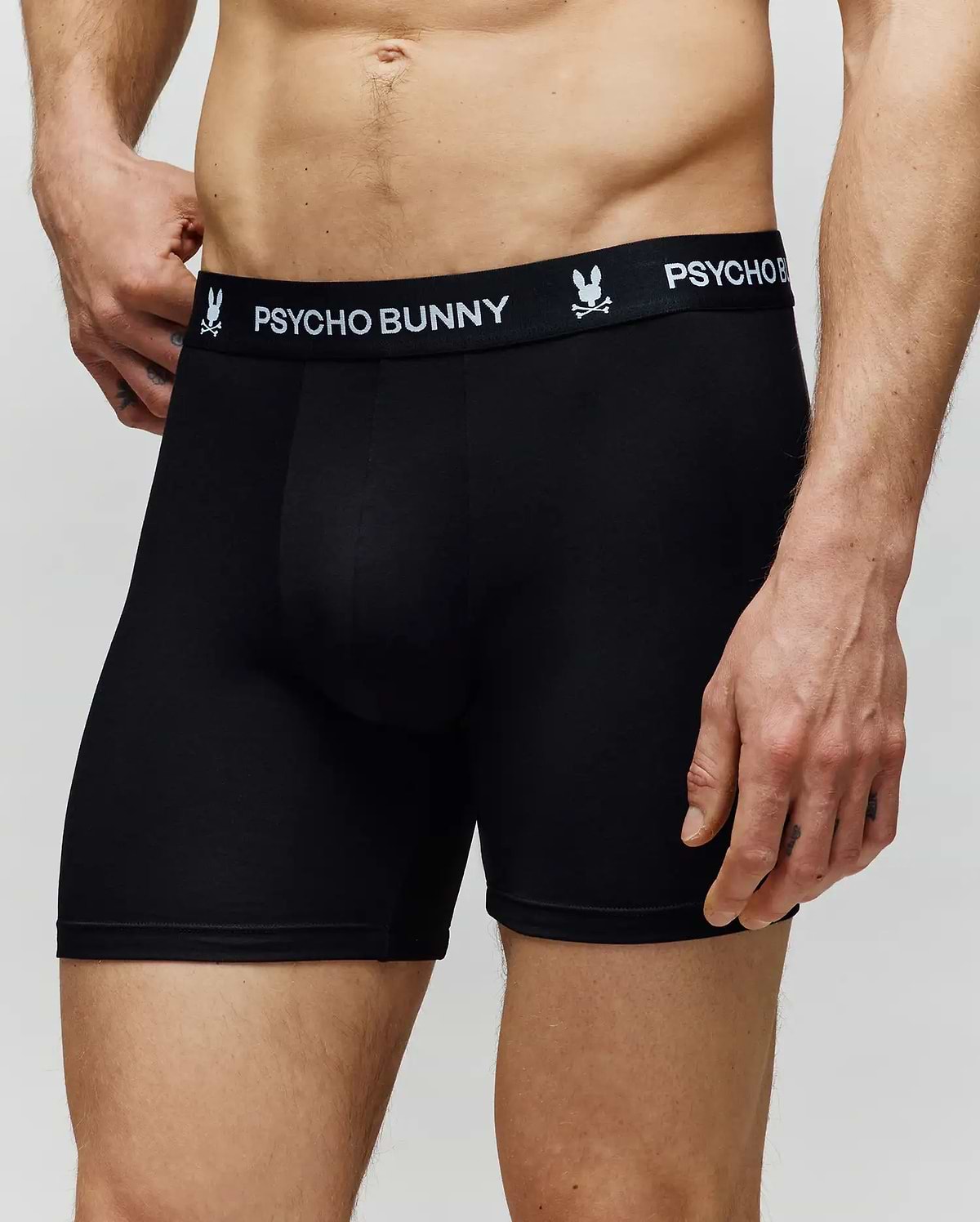 A man wears Psycho Bunny’s MENS 3 PACK BOXER BRIEF - MO1400006, featuring the brand's logo and bunny graphic on the waistband, made from a cotton-modal blend. Only his torso and upper legs are visible against a plain light background.