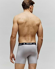 A man stands with his back to the camera, wearing Psycho Bunny MENS 3 PACK BOXER BRIEF - MO1400006 in light gray with a black "PSYCHO BUNNY" waistband, set against a plain neutral background.