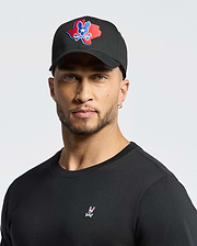 A man dons Psycho Bunny's MENS TEXAS BASEBALL CAP - MO1500014 with a colorful logo and a black cotton shirt embellished with a small design, set against a plain white background.