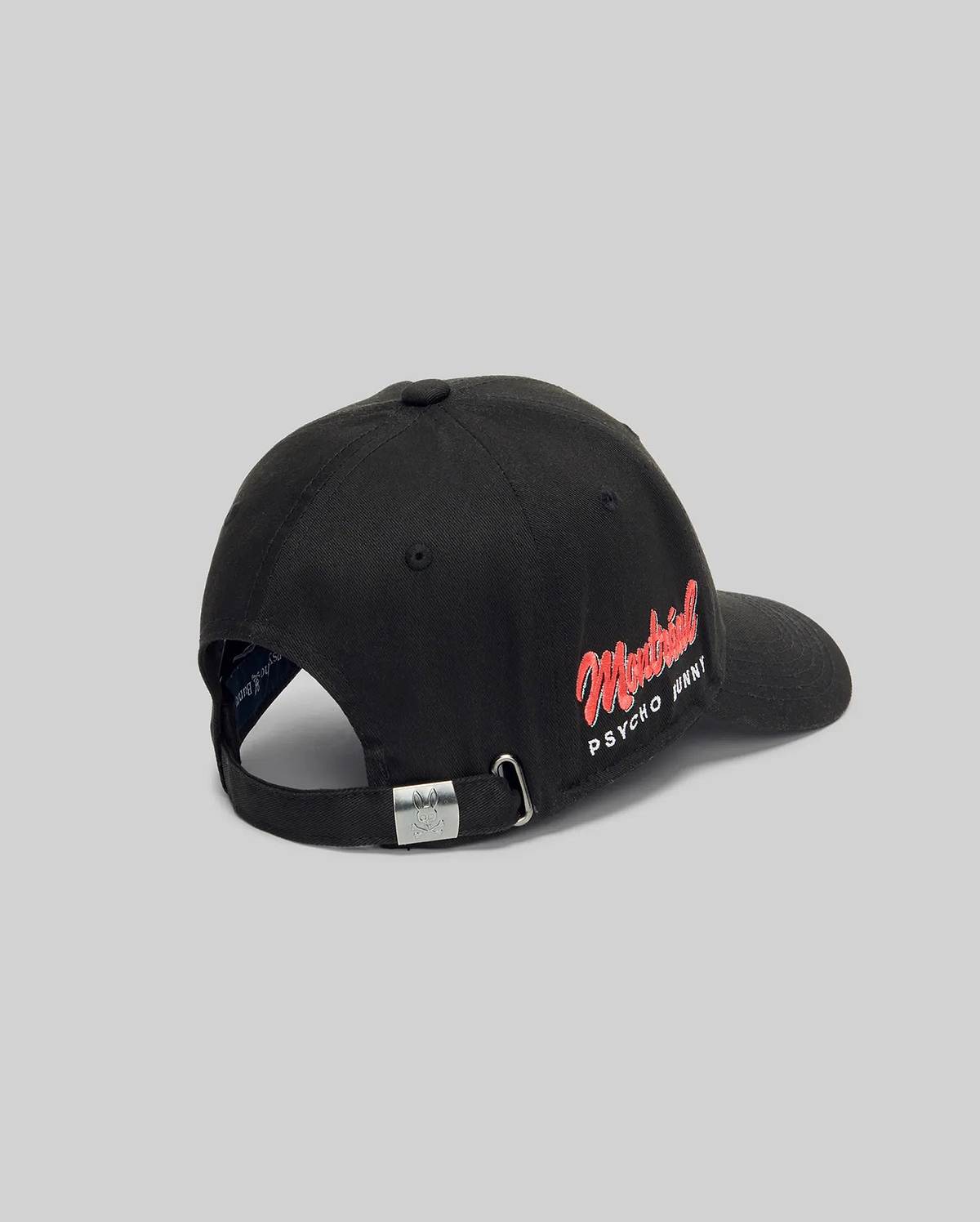 The Psycho Bunny MENS MONTREAL BASEBALL CAP (MO1500048) is a black 100% cotton cap with "Montreal PSYCHO PRINT" embroidered in red and white on the back left, plus an adjustable strap and metal buckle, shown on a light gray background.