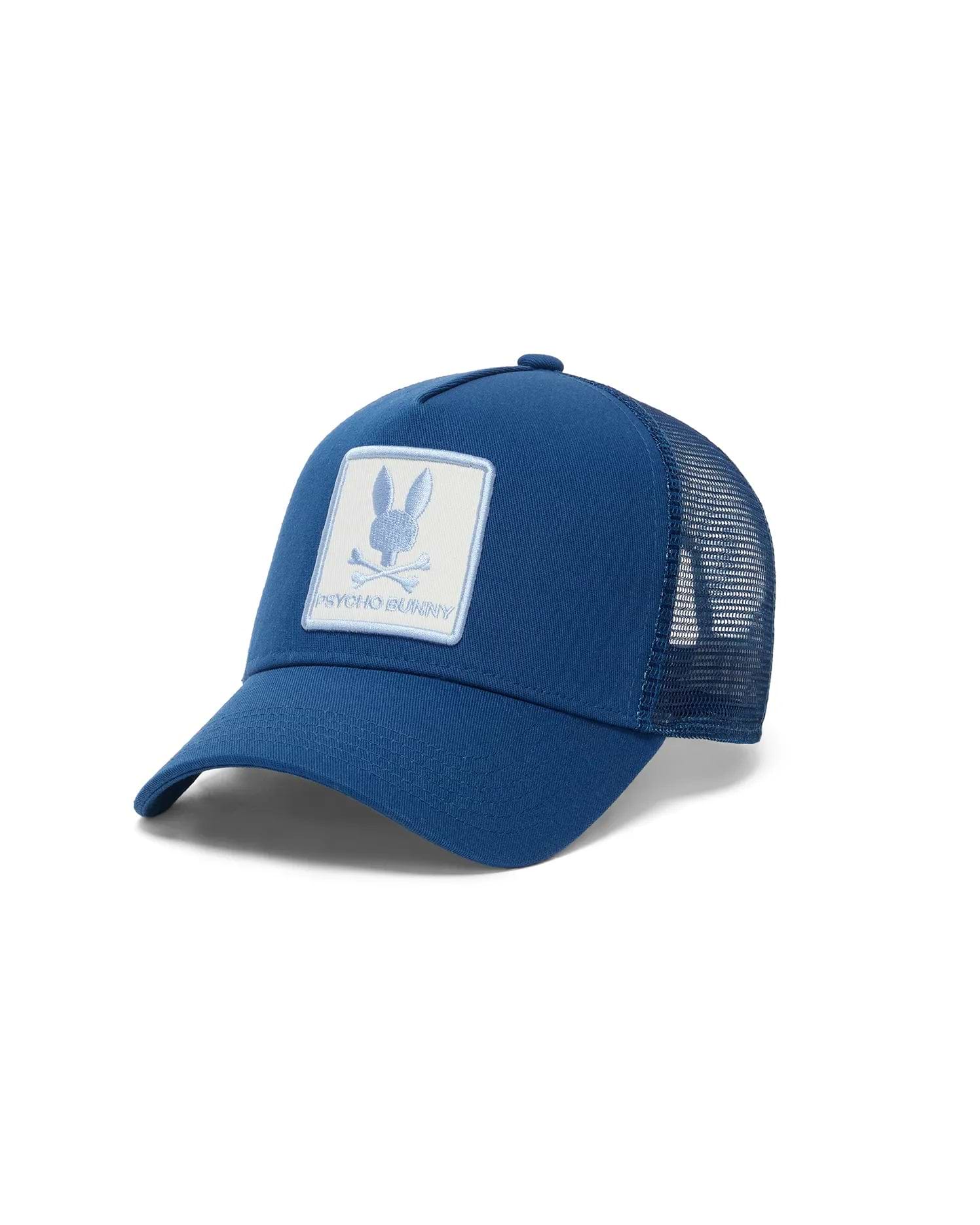 Mens Adamo Bunny Trucker Cap in royal blue, featuring solid front panels and a breathable mesh back. A large embroidered white patch on the front displays the light blue Psycho Bunny skull logo and text.