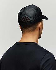 Mens Adamo Trucker Cap, a black cap with breathable mesh back panels and an adjustable snapback closure, paired with a classic fit black jersey knit crewneck t-shirt.