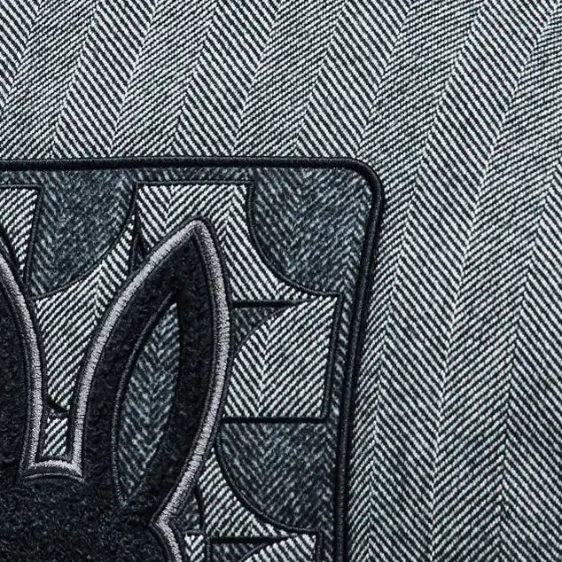 Grey herringbone jacket with black ribbed collar and large embroidered Psycho Bunny skull logo on back, paired with a black Jimmy Baseball Cap featuring a metal logo buckle.