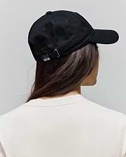 Black Jimmy Baseball Cap with a classic fit, featuring a silver adjustable buckle engraved with a small Psycho Bunny skull logo, worn over a cream jersey t-shirt.