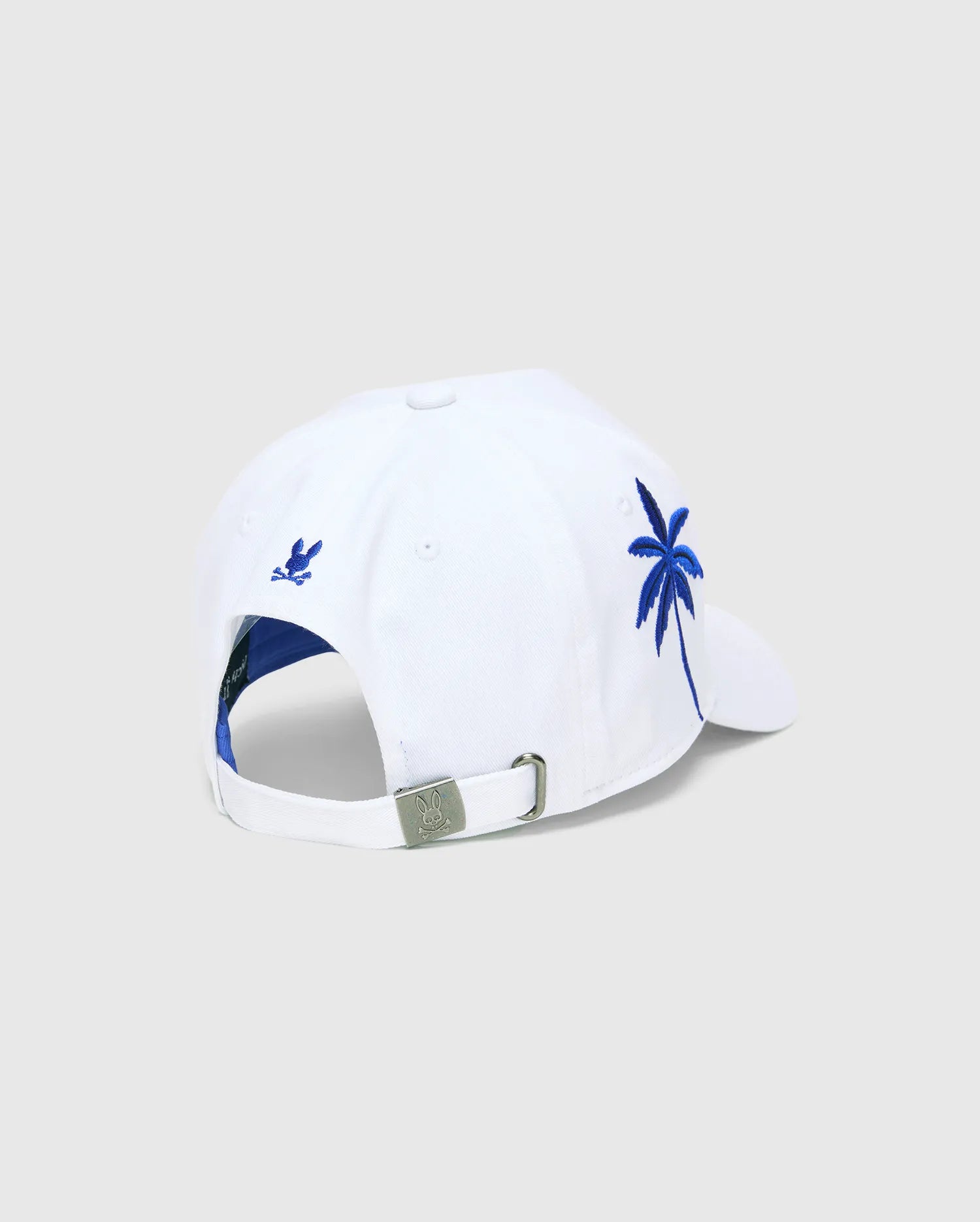 White Mens Brad Trucker Cap with blue interior, featuring a vibrant blue embroidered palm tree on the side, a small blue embroidered Psycho Bunny skull on the back, and a branded metal buckle.