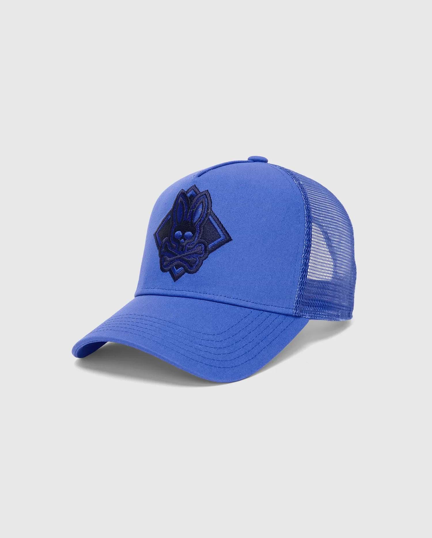Mens Tobias Trucker Cap in royal blue, featuring a cotton twill front and breathable mesh back. A large, central embroidered dark blue Psycho Bunny skull logo is set within a diamond on the front.