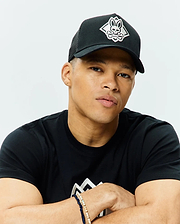 Black Mens Tobias Trucker Cap with a white embroidered Psycho Bunny skull and crossbones logo on the front, featuring a mesh back. Worn with a black classic fit jersey t-shirt displaying a large white geometric chest graphic.