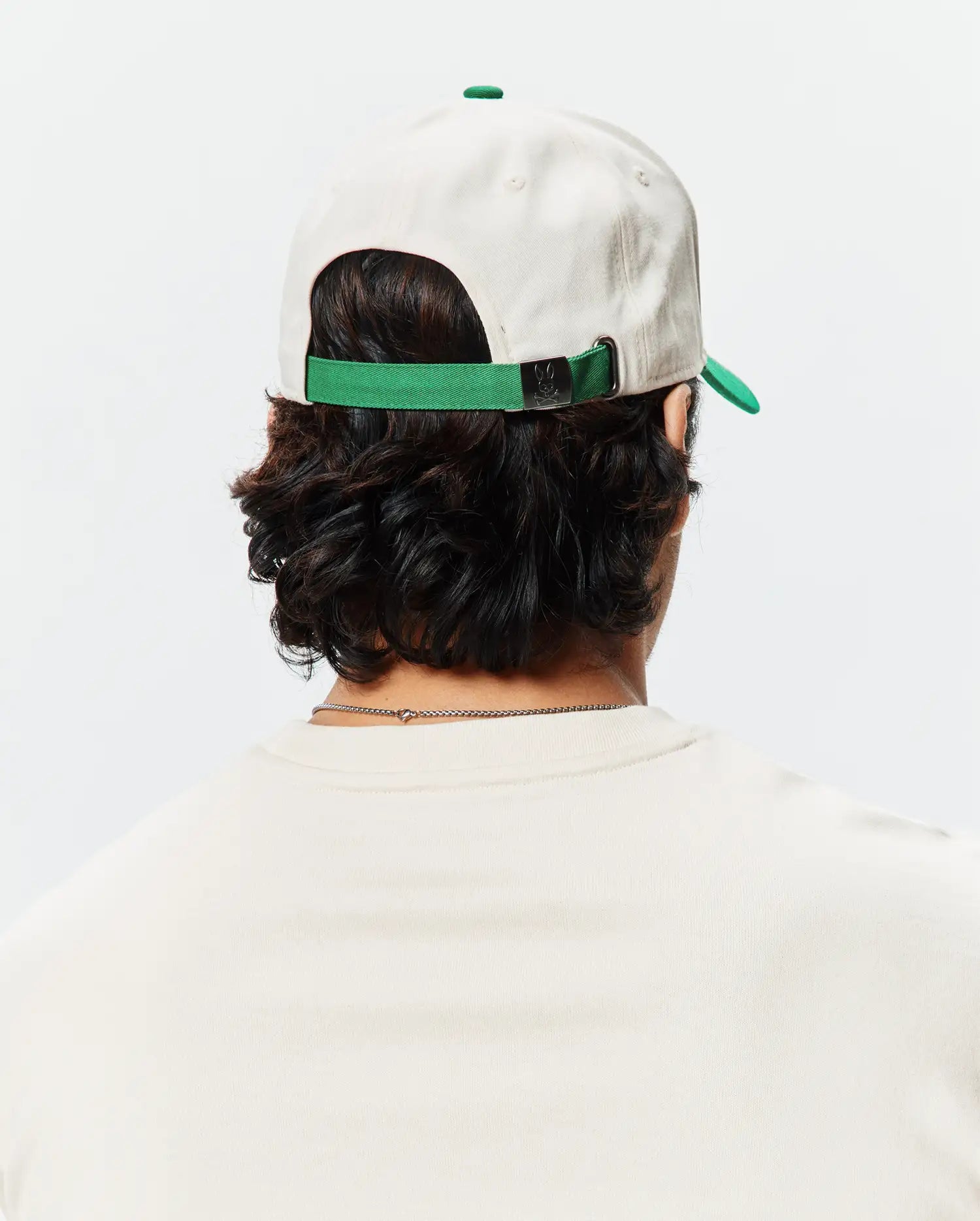 Mens Craig Baseball Cap in cream cotton twill with a green brim and adjustable strap featuring a small Psycho Bunny skull logo on the metal buckle.