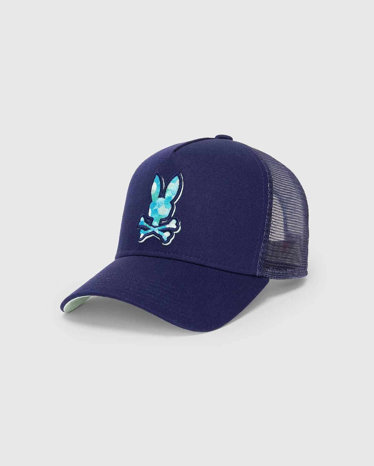 Mens Ethan Trucker Cap in navy blue, featuring a large, embroidered Psycho Bunny skull logo with a blue and teal patterned fill on the front, mesh back, and a light green underbrim.