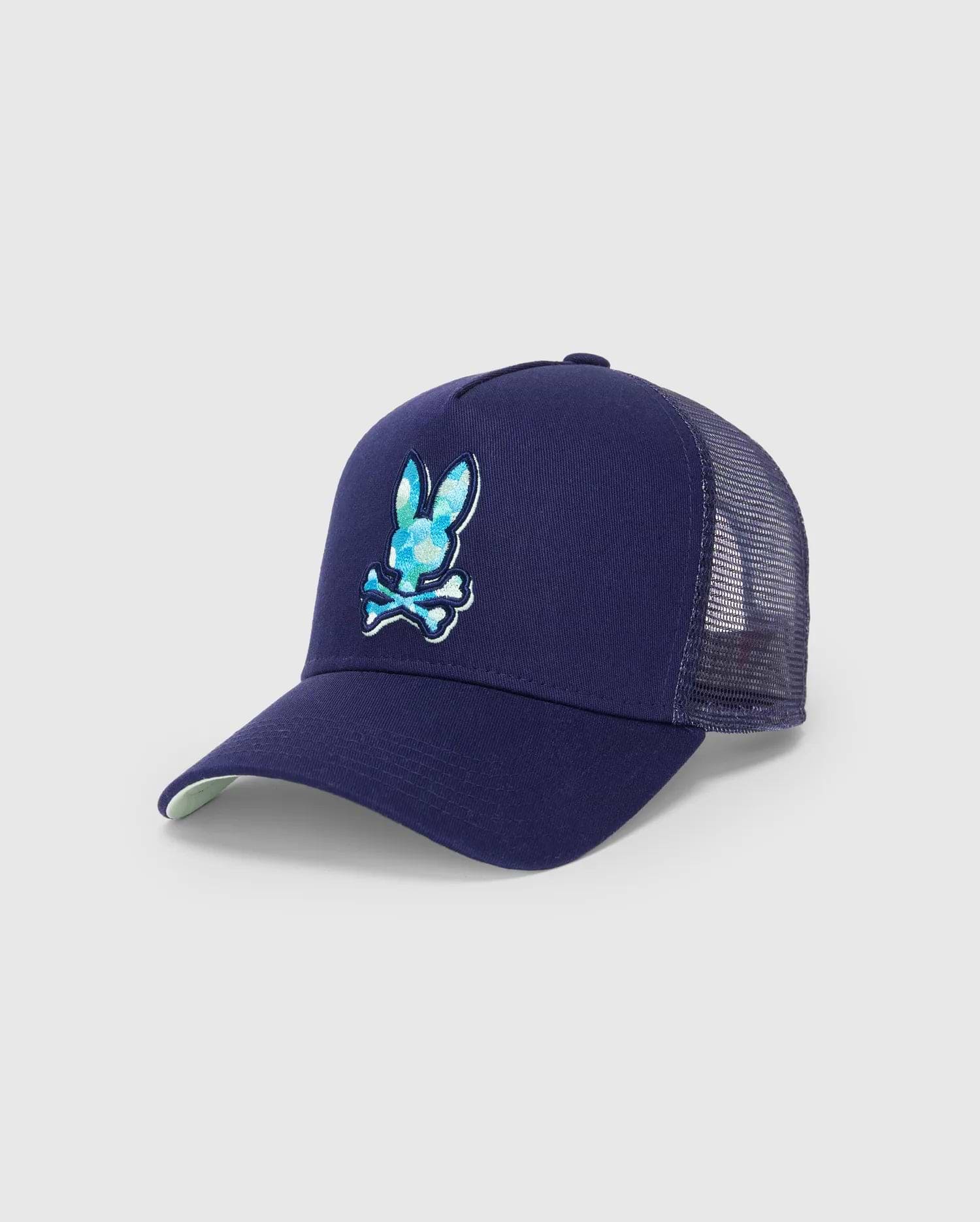 Mens Ethan Trucker Cap in navy blue, featuring a large, embroidered Psycho Bunny skull logo with a blue and teal patterned fill on the front, mesh back, and a light green underbrim.
