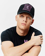 Black Mens Frank Trucker Cap with large pink embroidered Psycho Bunny skull and chain logo, paired with a black jersey crew neck t-shirt featuring a large pink embroidered Psycho Bunny logo on the left chest.