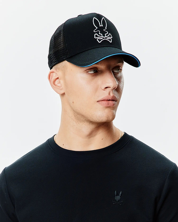 Black Mens Apollo Trucker Cap with mesh back, white embroidered Psycho Bunny skull logo, blue brim accent, and a black pique long-sleeve shirt with a small black embroidered Psycho Bunny logo on the left chest.