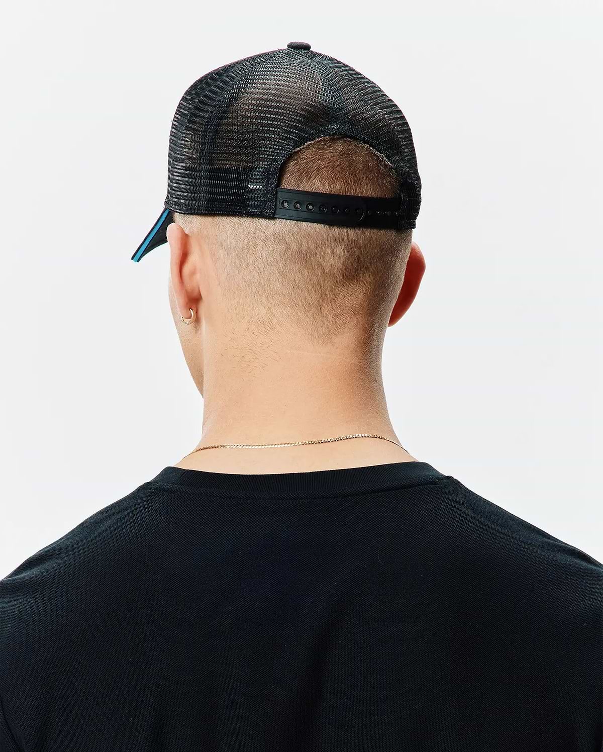 Black Mens Apollo Trucker Cap with breathable mesh back, adjustable snapback closure, and a subtle blue accent under the brim, worn with a classic fit black knit t-shirt.