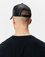 Black Mens Apollo Trucker Cap with breathable mesh back, adjustable snapback closure, and a subtle blue accent under the brim, worn with a classic fit black knit t-shirt.