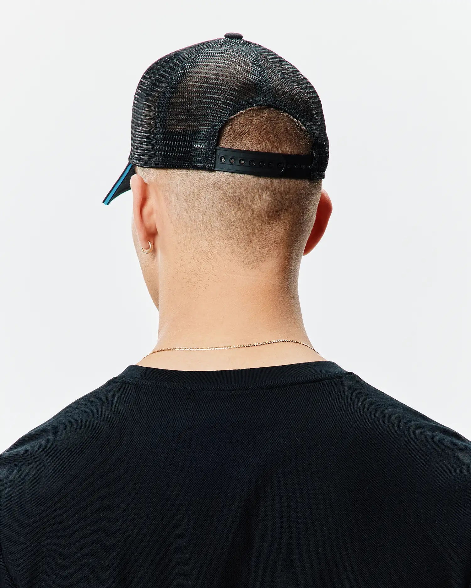 Black Mens Apollo Trucker Cap with breathable mesh back, adjustable snapback closure, and a subtle blue accent under the brim, worn with a classic fit black knit t-shirt.