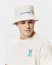 Mens Frank Reversible Bucket Hat in beige with blue Psycho Bunny embroidery and a vibrant patterned underside, paired with an off-white jersey t-shirt featuring a large teal and orange Psycho Bunny skull logo on the left chest. (3)