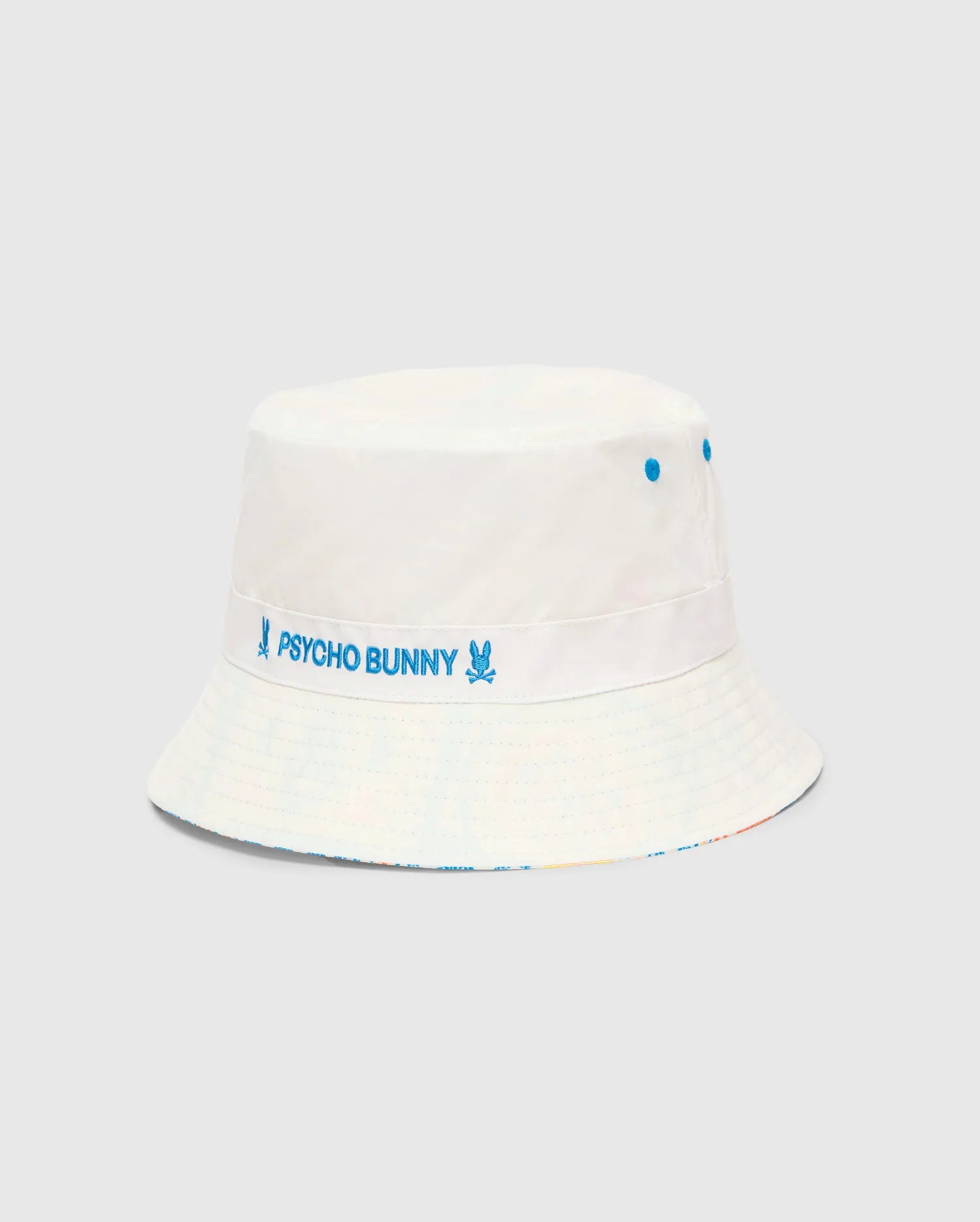 Mens Frank Reversible Bucket Hat in white, featuring a prominent blue embroidered Psycho Bunny text and skull logo band, blue ventilation eyelets, and a subtle multicolor pattern on the reversible side. (4)