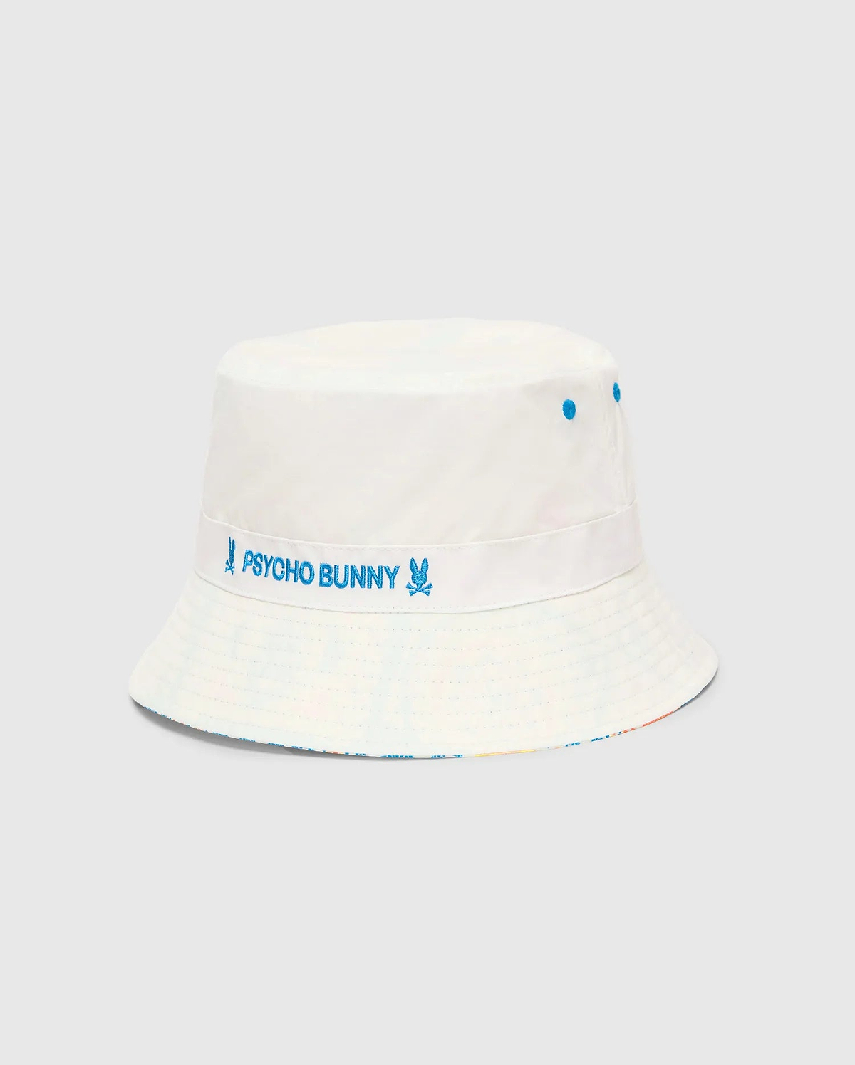 Mens Frank Reversible Bucket Hat in white, featuring a prominent blue embroidered Psycho Bunny text and skull logo band, blue ventilation eyelets, and a subtle multicolor pattern on the reversible side. (4)